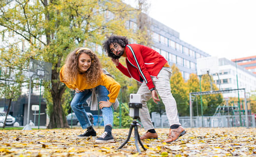 Preview: Young couple with smartphone making video for social media outdoors in park.