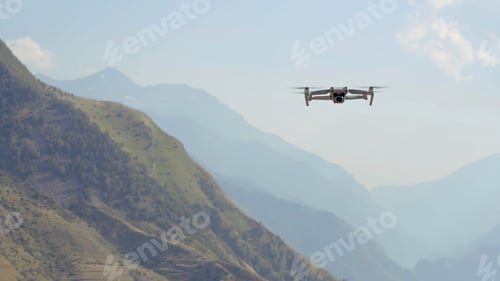 Preview: Aerial view of a quadcopter flying above green mountains on morning haze background. Action. Drone