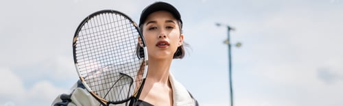 Preview: banner, woman in active wear and cap looking at camera and holding tennis racket on court, sport