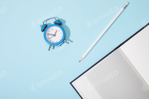 Preview: top view of classic alarm clock with blank netbook and pencil on blue background