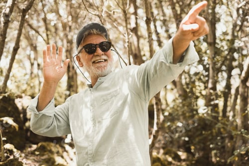 Preview: Happy senior smiling man in sunglasses enjoying hiking in the forest. Elderly attractive bearded man