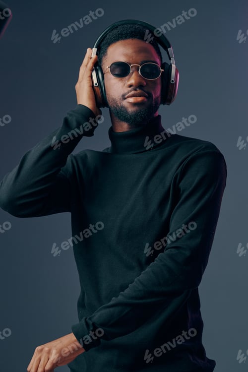 Preview: Stylish African man in black turtleneck and sunglasses enjoying music with headphones, conveying
