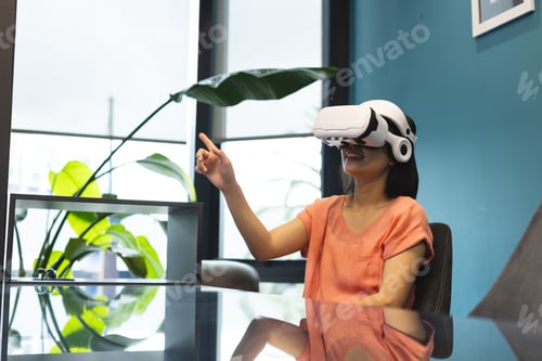 Preview: A young Asian woman wearing VR headset is pointing at something in a modern business office