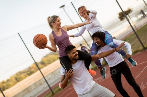 Preview: Young women sitting on the men shoulders and holding a basketball at outdoor court
