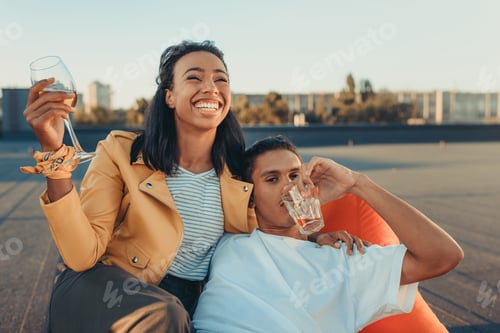 Preview: young couple with glasses of alcohol relaxing on roof