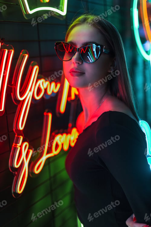 Preview: Happy beautiful fashion girl with stylish glasses near multicolored neon lights