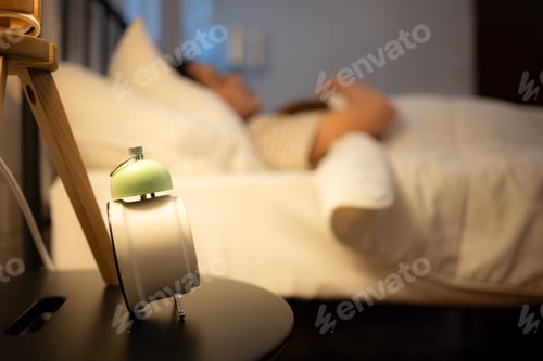 Preview: Alarm clock on a bedside table with woman sleeping in the background
