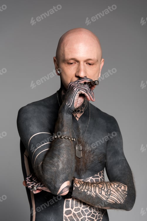 Preview: bald shirtless man with tattoos smoking cigar and looking down isolated on grey