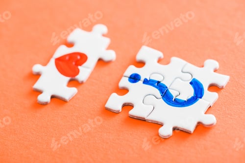 Preview: selective focus of connected puzzle pieces with drawn red heart and blue question mark on orange