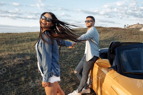 Preview: Happy young couple staying beside a yellow convertible car. Adventure, travel and love concept.