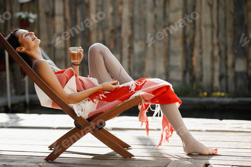 Preview: Young woman wrapped in a red and white plaid sits in a folding chair with glass of water in her hand