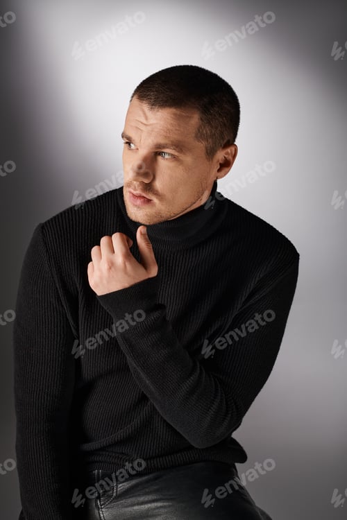Preview: thoughtful handsome stylish man in black turtleneck looking away on grey backdrop with lighting