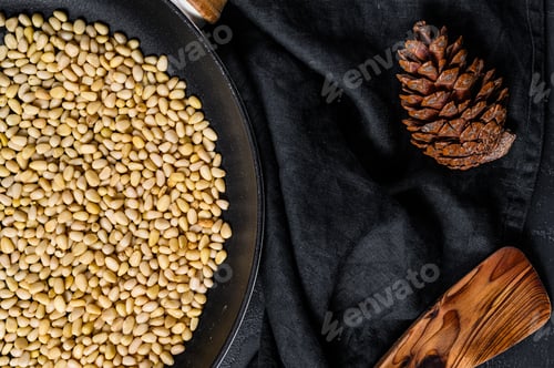 Preview: Roasted pine nuts in a frying pan. Black background. Top view