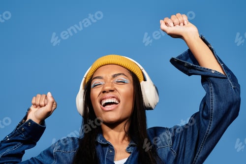 Preview: A young woman enjoys music outdoors in stylish autumn attire under a clear blue sky