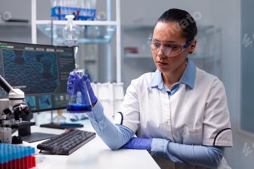 Preview: Scientist woman doctor holding glass flask analyzing liquid solution working at biochemistry