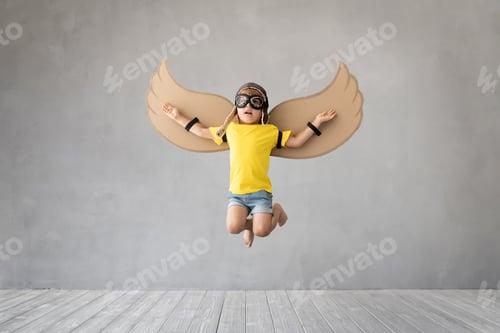 Preview: hild with paper wings jumping against grey concrete background