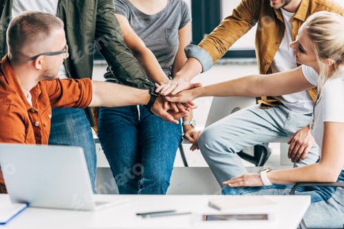 Preview: cropped shot of group of young entrepreneurs making team gesture while working on startup together