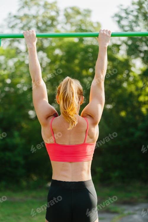 Preview: Woman exercising outdoors, pulling up on horizontal bar