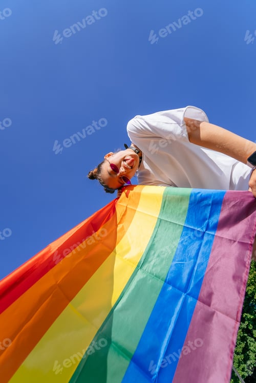 Preview: A young woman develops a rainbow flag against the sky