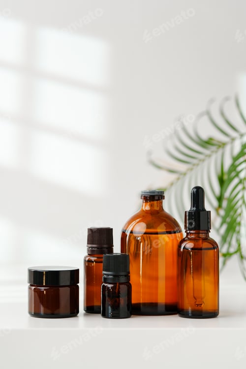 Preview: Collection of Amber Glass Bottles and Jars for Essential Oils on a White Surface