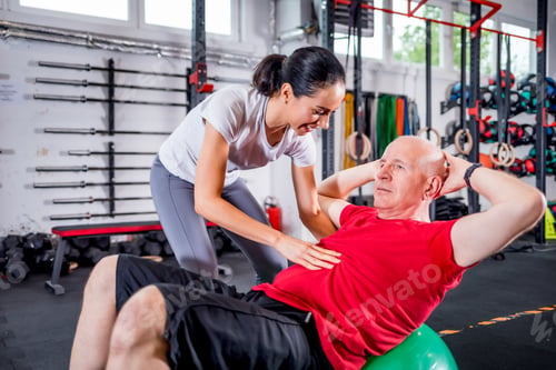 Preview: Senior man with trainer doing rehab using pilates ball in the rehabilitation center