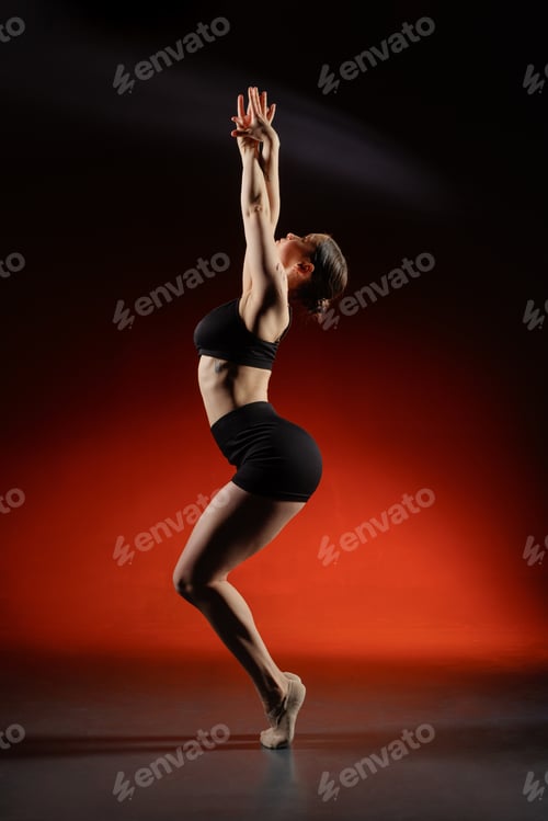 Preview: Female dancer stretching on toes in studio with red background and copy space