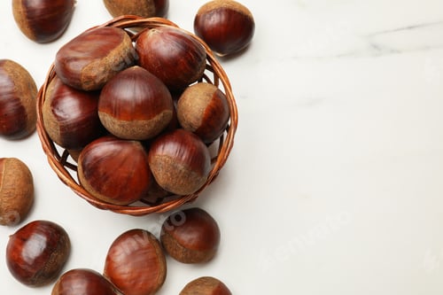 Preview: Sweet fresh edible chestnuts in wicker bowl on white marble table, top view. Space for text