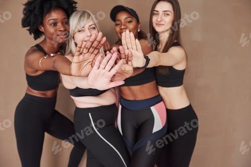 Preview: Focused photo. Group of multi ethnic women standing in the studio against brown background