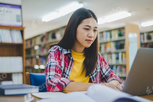 Preview: Female college student working on laptop and searching for books to study