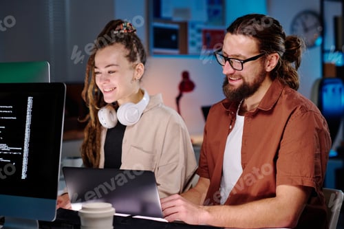 Preview: Two happy young IT managers sitting by workplace in front of computer screens