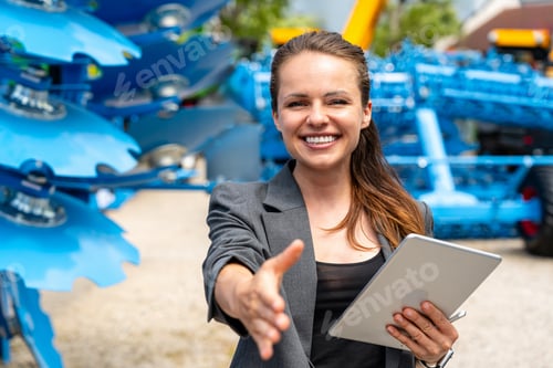 Preview: Female agricultural sales representative offering handshake at outdoor equipment dealership