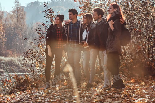 Preview: Group of young friends hugging together and lookina away in beautiful autumn forest.