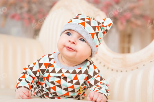 Preview: Baby, childhood and newborn concept - little child lying on the couch in the coloured cap.