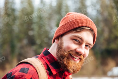 Preview: Happy man with beard in hat and checkered shirt outdoors