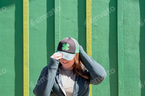 Preview: Young woman wearing a shamrock hat standing in front of a green wall on St. Patrick’s Day
