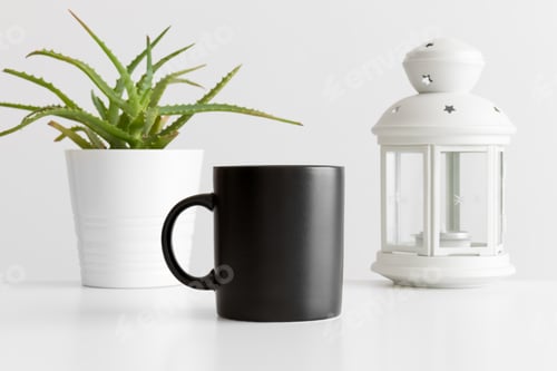 Preview: Black mug mockup with a candle holder and a aloe vera plant on a white table.