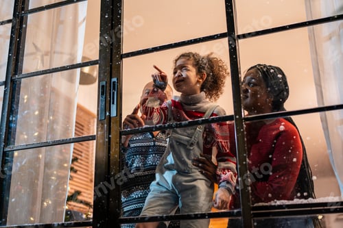 Preview: Adorable child looking at the window and first snow flakes with family.