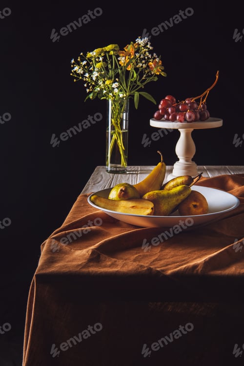 Preview: plate of pears and stand with grapes and vase of flowers on table on black