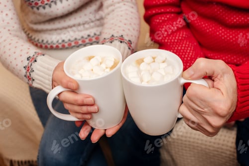 Vista previa: vista recortada de pareja sosteniendo dos tazas de cacao con malvaviscos en la víspera de Navidad