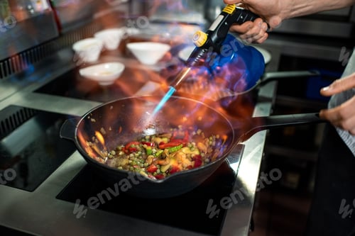 Preview: Hand of young chef using electric smoker for chopped vegetables in frying pan