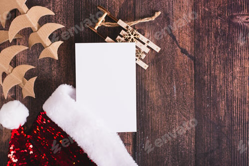 Preview: List of gifts with santa claus hat, cardboard fir trees and sleigh on the table top view