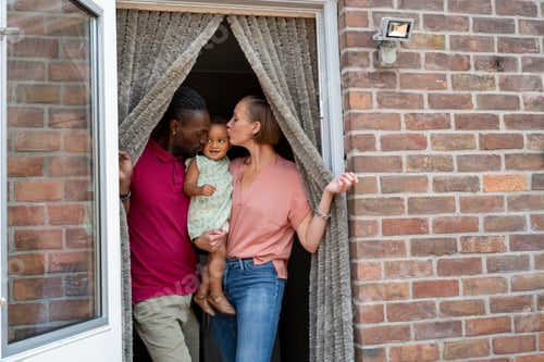 Preview: Family with a toddler smiling at each other in a doorway with a brick wall background.