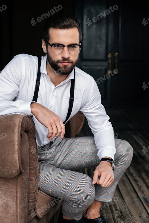 Preview: elegant bearded man in eyeglasses sitting in armchair