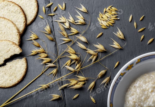 Preview: High angle shot of branches of wheat, fresh bread, and porridge on a grey surface