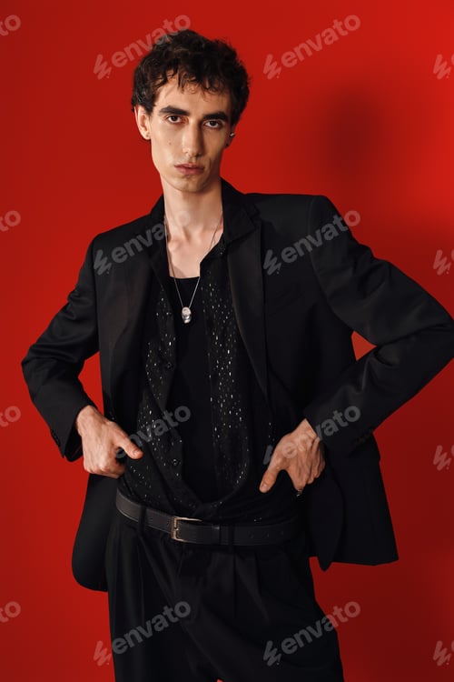 Preview: Handsome man showcasing elegance and style in a striking black outfit against a vibrant red backdrop