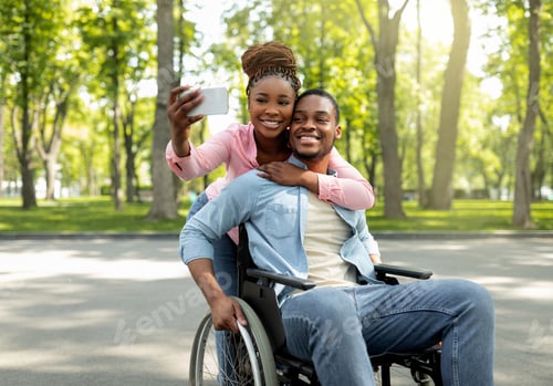 Preview: Happy black woman and her impaired boyfriend in wheelchair taking selfie together, hugging at city