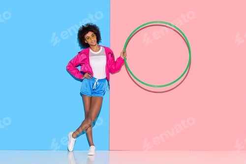 Preview: Woman in sportswear standing with hoop in hand on pink and blue background