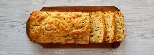 Preview: Homemade Cheesy Bread Loaf on a rustic wooden board on a white wooden background, top view.