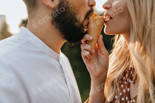 Preview: Portrait of romantic couple in park biting mango ice cream from different sides