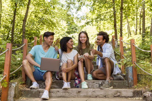 Preview: Multiethnic friends students outdoors using mobile phone and laptop